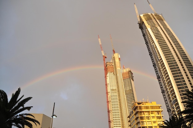 Arco-íris sobre o céu nublado e chuvoso com arranha-céus e torre alta residencial à noite