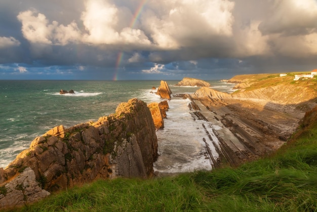 Foto arco iris sobre la playa de la arnia en santander cantabria norte de españa con acantilados y rocas flysch