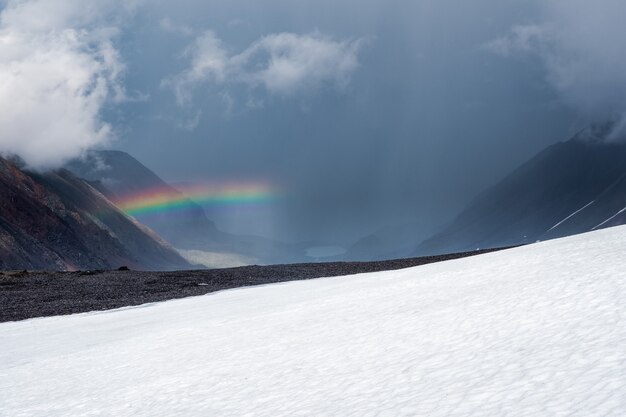 Arco iris sobre un valle de montaña de nieve de invierno. Paisaje alpino atmosférico con montañas nevadas con arco iris en tiempo lluvioso y soleado.