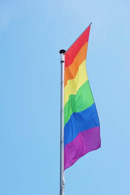 Arco iris vertical o bandera del orgullo lgbt en el asta de la bandera contra el cielo azul claro