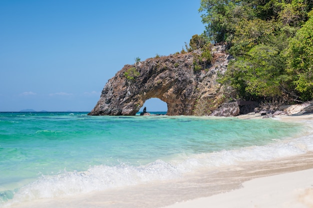 Arco natural de roca sobre mar turquesa y la playa.