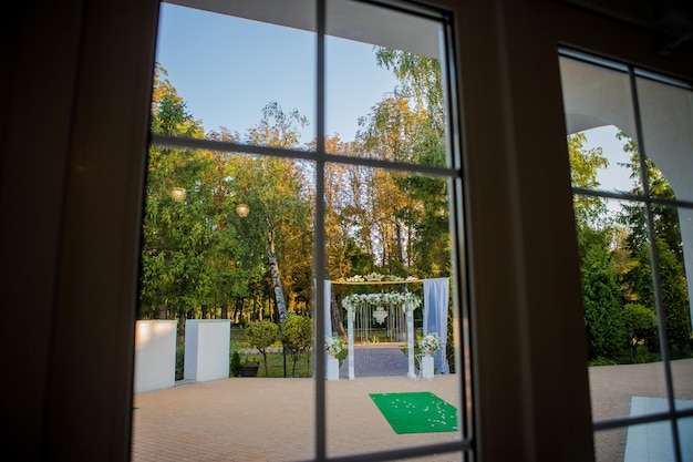 Arco para a cerimônia de casamento O arco é decorado com um pano, um lustre de cristal e flores Vista do arco de casamento da janela Decorações de casamento