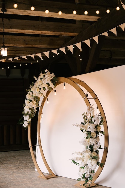 Arco redondo de madeira com fundo branco e decorado com flores e guirlanda retrô