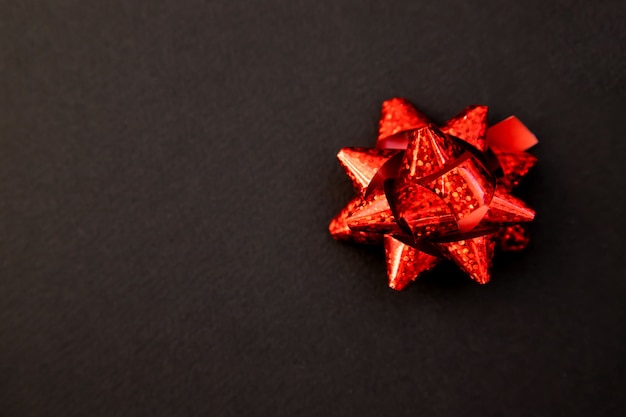 Arco de regalo en rojo sobre fondo negro. Navidad y año nuevo. Un regalo de cumpleaños. Espacio vacío para el texto.