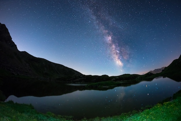 Arco de la Vía Láctea y cielo estrellado reflejado en el lago a gran altitud en los Alpes