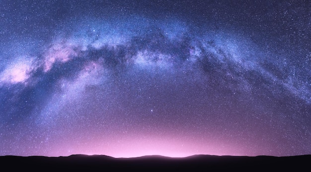 Arco de la Vía Láctea Fantástico paisaje nocturno con un brillante cielo arqueado de la Vía Láctea púrpura con estrellas, luz rosa y colinas Hermosa escena con el universo Fondo espacial con cielo estrellado Galaxia y naturaleza