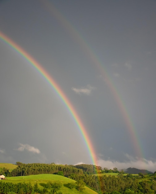 Foto un arcoíris y su reflejo en un paisaje de verdes prados en cantabria (españa)