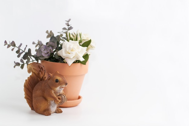 Ardilla de cerámica y olla de barro con rosas sobre un fondo blanco con un lugar para el texto