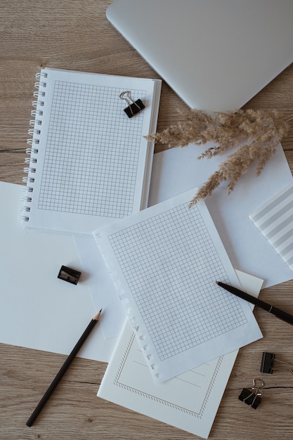 Área de trabalho da mesa do escritório doméstico com folhas de papel em branco, laptop, caderno, grama dos pampas