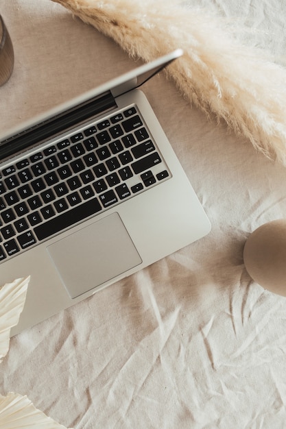 Área de trabalho da mesa do escritório doméstico com laptop, folhagem de junco na toalha de mesa de linho bege