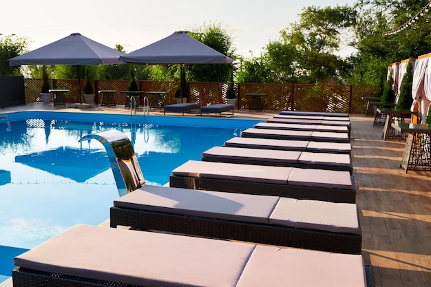 Foto Área de la piscina con sillas de sol y sombrillas a lo largo de la piscina en un complejo de lujo camas de playa rodeadas de vegetación y agua azul tranquilidad y atmósfera de relajación en vacaciones