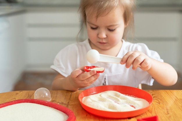 Areia arte terapia garotinha pintada em uma mesa com areia Brincadeiras sensoriais em casa brincando na sêmola na cozinha desenvolvimento de habilidades motoras finas Atividades Montessori