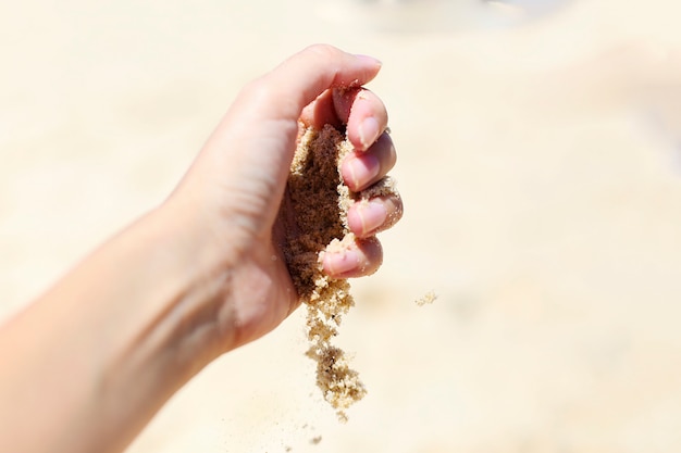 Areia correndo pela mão da mulher na praia