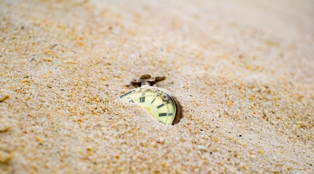 Foto areia do tempo relógio de bolso antiquado podre enterrado parcialmente na areia