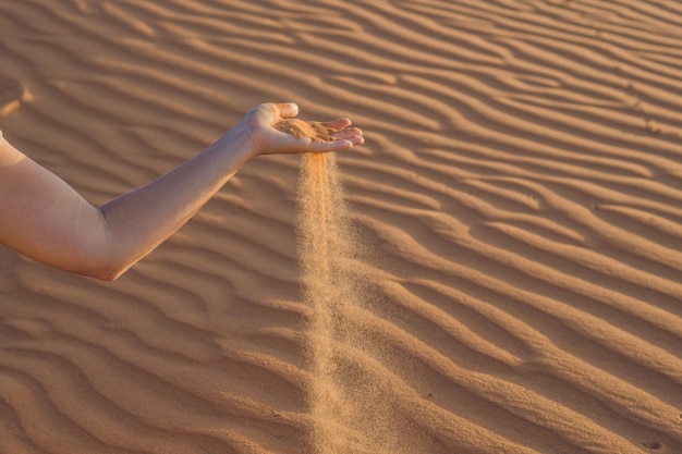 Areia escorregando pelos dedos da mão de uma mulher no deserto