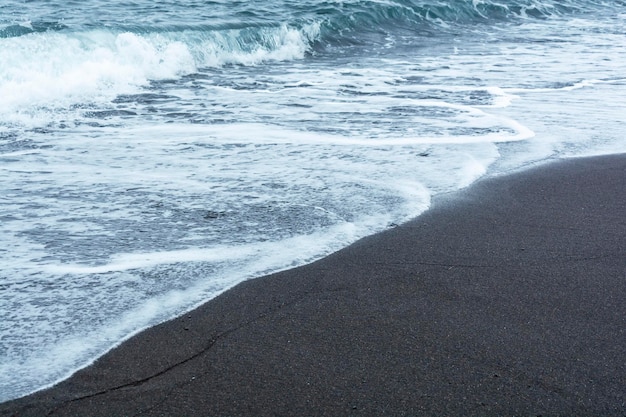 Areia vulcânica preta na praia com ondas