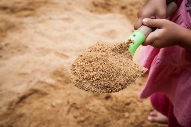 Arena en el juguete, niña con pala de arena en el patio