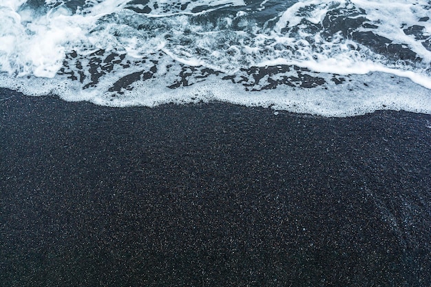 Arena volcánica negra en la playa con olas