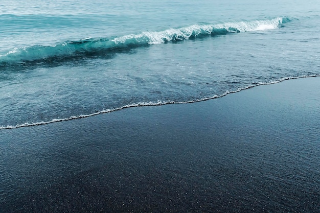 Arena volcánica negra en la playa con olas