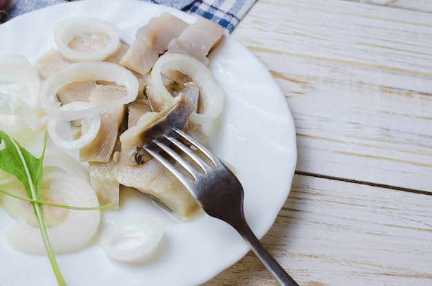 Arenque con cebolla en plato blanco.