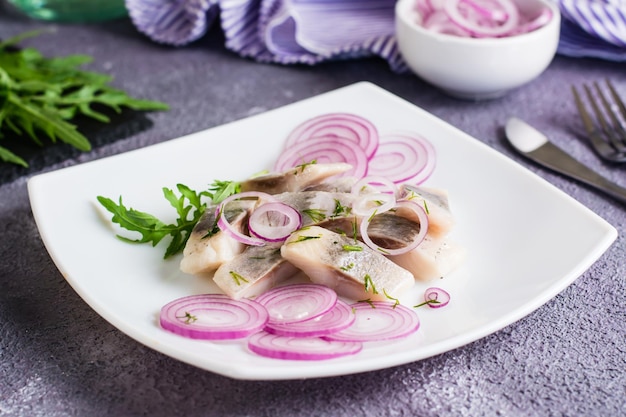 Arenque salado en rodajas con cebolla y rúcula en un plato sobre la mesa Merienda simple