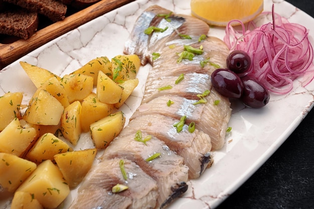 Arenque salgado com batatas cebolas azeitonas limão e torradas em um fundo escuro