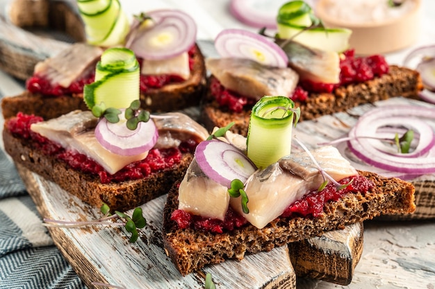 Arenque tradicional matie com salada de beterraba pepino fresco e anéis de cebola nas torradas na chapa branca cozinha escandinava