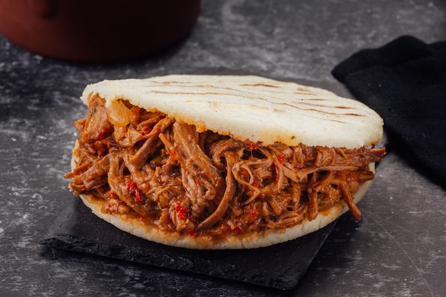 Arepa gefüllt mit geschreddertem Fleisch auf dunklem Hintergrund. (Arepa con carne mechada)