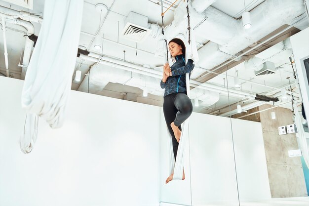 Ariel Yoga junge kaukasische Frau in Sportkleidung, die Fliegenyoga im Studio praktiziert, das auf dem steht