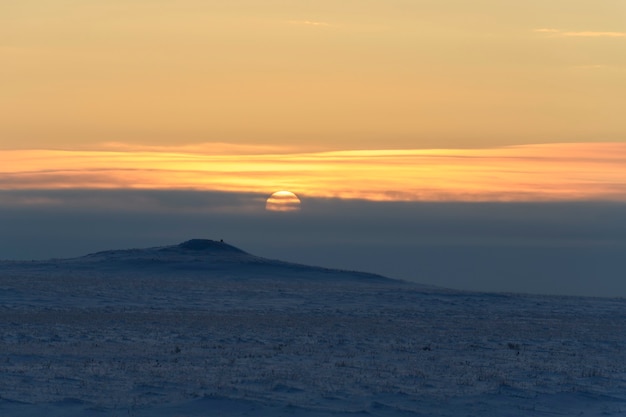 Arktische Landschaft im Winter. Kleiner Fluss mit Eis in der Tundra. Sonnenuntergang.