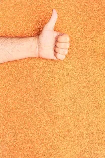 Foto arm mit daumen nach oben handgeste oben mit glitzerndem orangefarbenem hintergrund