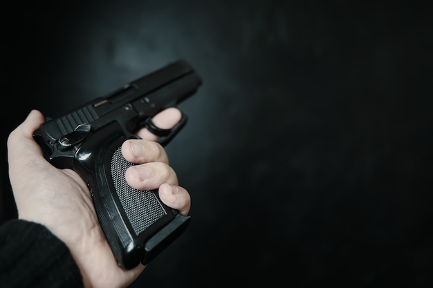 Arma de fogo na mão do homem, visão em primeira pessoa do criminoso armado com pistola na defesa de fundo preto ou ...