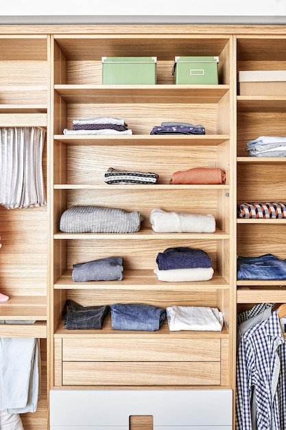 Armario moderno de madera con ropa colgada en estantes deslizables y doblada en los estantes