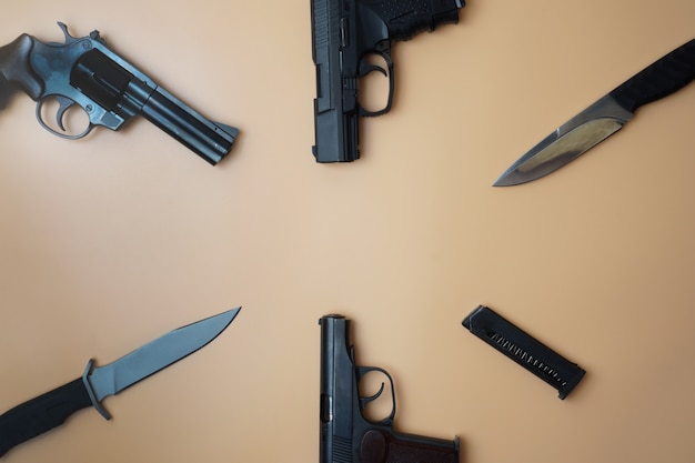 Armas de fogo dispostas ao longo de um círculo. três armas, pistolas, cartuchos, close-up de canivetes em um fundo bege neutro.