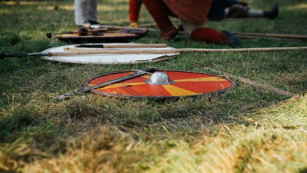 Armas medievales un escudo redondo rojo y una espada de acero en el campo de batalla al aire libre Enfoque selectivo