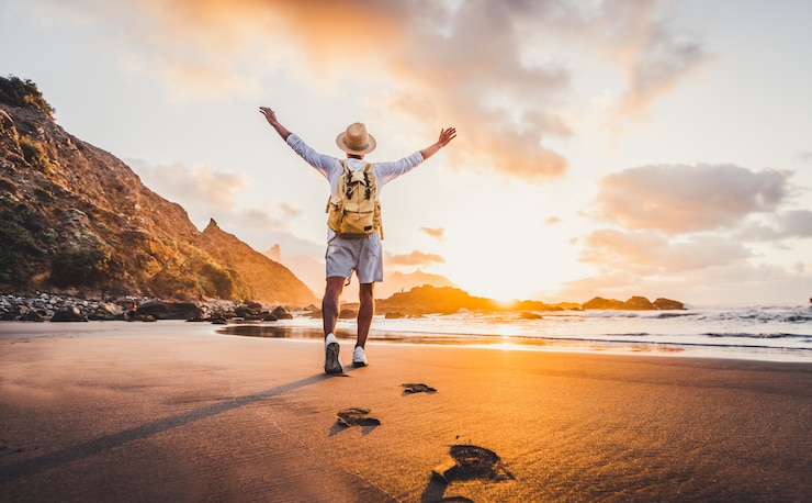 Foto arme des jungen mannes, die bei sonnenaufgang vom meer ausgestreckt werden und freiheit und leben genießen, reisen menschen wohlbefinden konzept