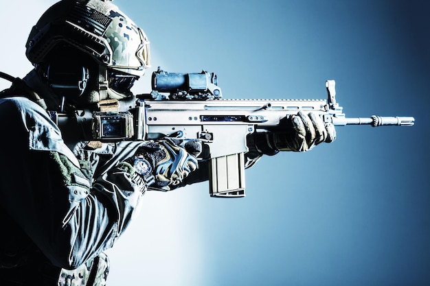 Armeesoldat in schützender Kampfuniform, die Special Operations Forces Combat Assault Rifle hält. Schusswaffe hautnah. Studioaufnahme, isoliert auf weißem Hintergrund