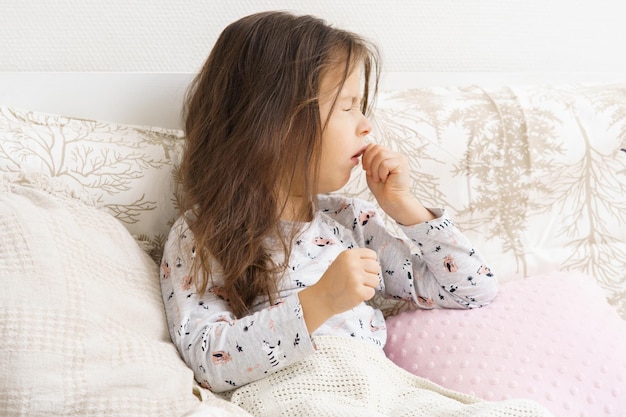 Armes unglückliches kleines brünettes Vorschulkind Mädchen im Schlafanzug hustend im weichen Bett liegend Halsschmerzen Angina