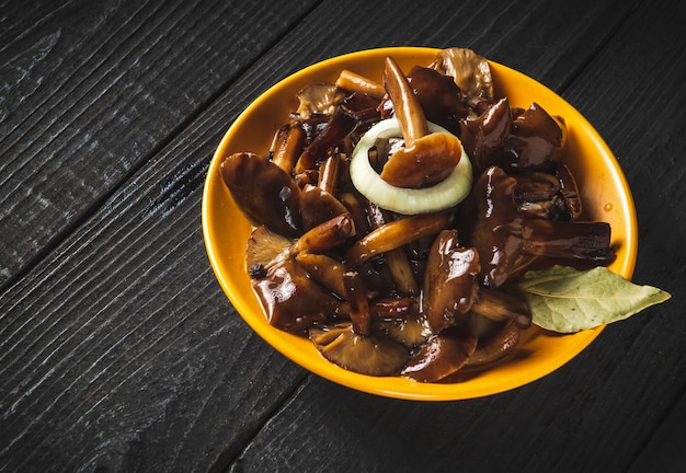 Armillaria mellea u hongo de miel marinado en un plato amarillo con especias y cebollas sobre una mesa vintage.