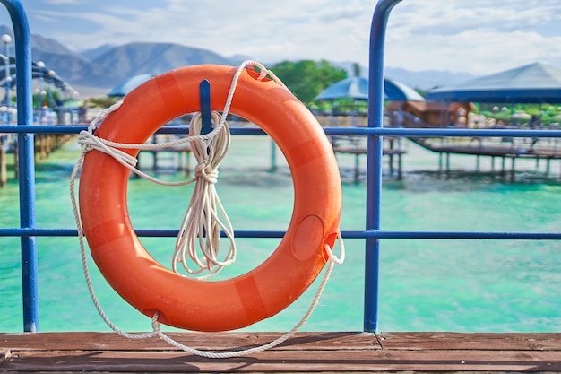 Aro salvavidas naranja con cuerda en un muelle de madera cerca del mar