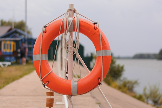 El aro salvavidas naranja está atado a una valla en el muelle del río. vista frontal