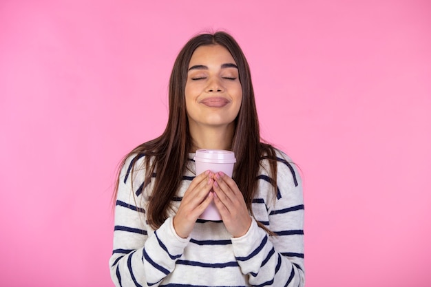 Aroma maravilloso. Foto de mujer satisfecha en suéter sostiene un vaso de papel de bebida caliente, cierra los ojos