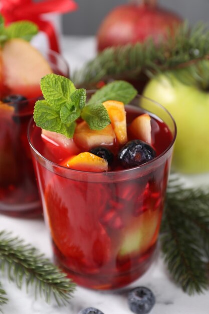Aromatisches Sangria-Getränk in Glas-Zutaten und Weihnachtsdekoration auf weißem Marmortisch
