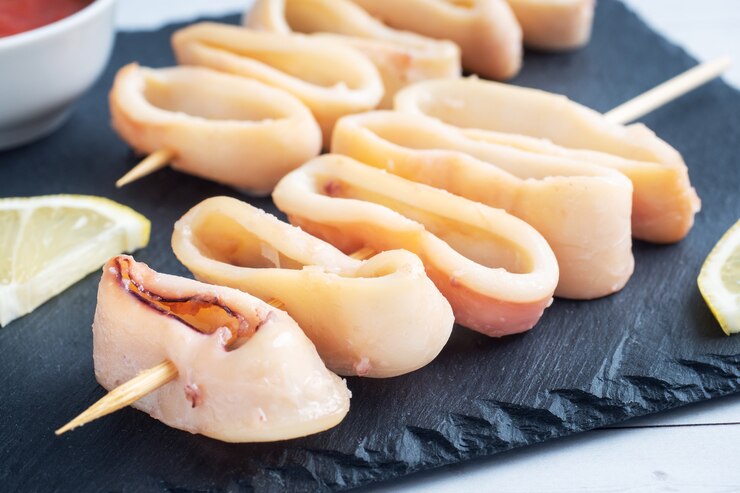 Aros de calamar fritos en brocheta con salsa de tomate y limón. Soporte de pizarra negra, de cerca.