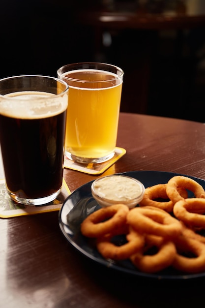 Aros de cebolla dorados crujientes espolvoreados con sal marina en un bol y vasos de cerveza en una mesa de madera