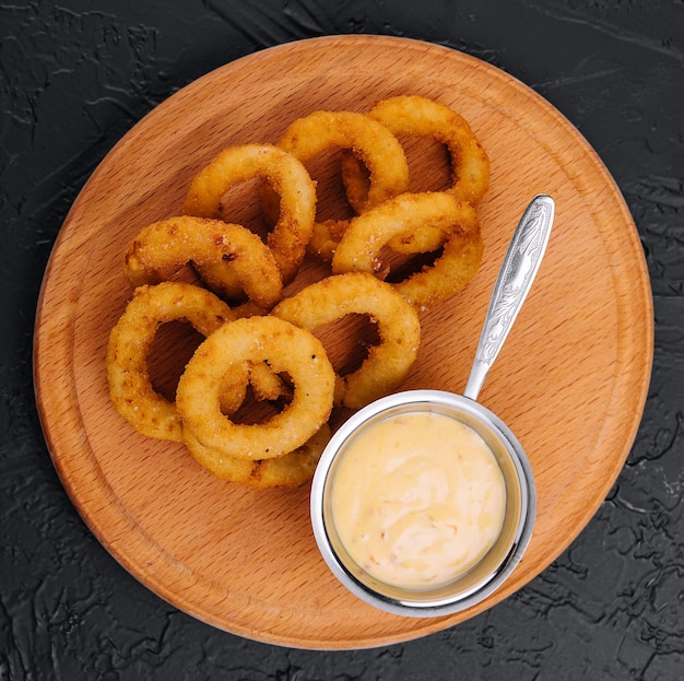 Aros de cebolla fritos crujientes y salsa en plato de madera