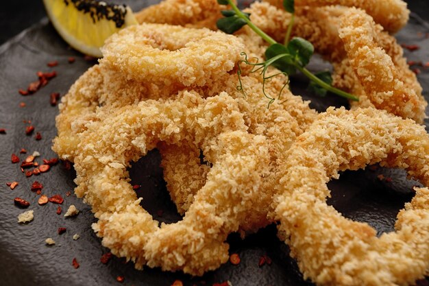 Aros de cebolla fritos rebozados con especias en un plato negro sobre un fondo negro