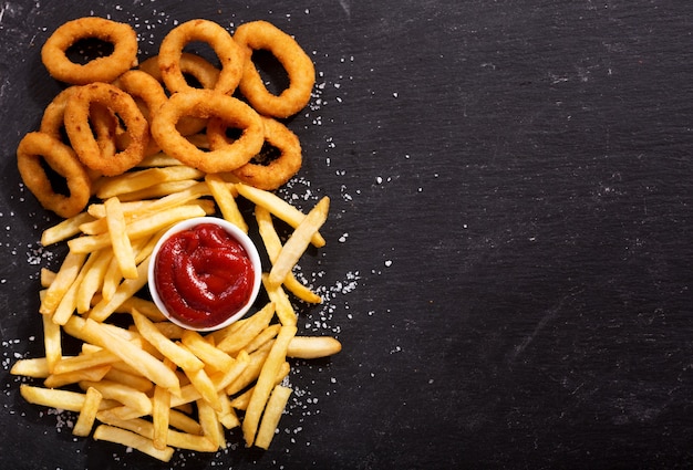 Aros de cebolla y papas fritas con salsa de tomate en la vista superior de la mesa oscura