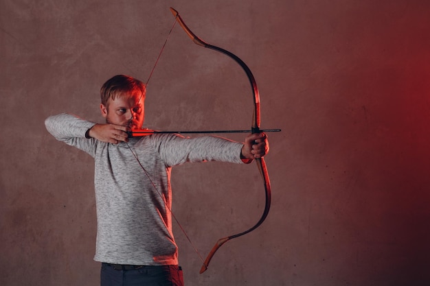 El arquero con el arco y la flecha asiáticos clásicos apunta en el estudio de luz roja apunta al objetivo