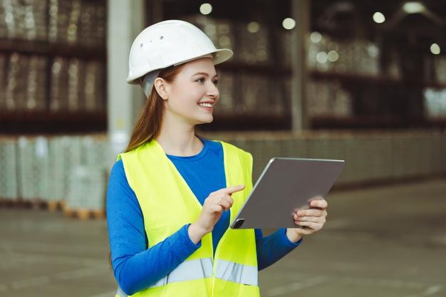 Arquitecta sonriente con sombrero blanco y ropa de trabajo sosteniendo una tableta digital usando una aplicación móvil